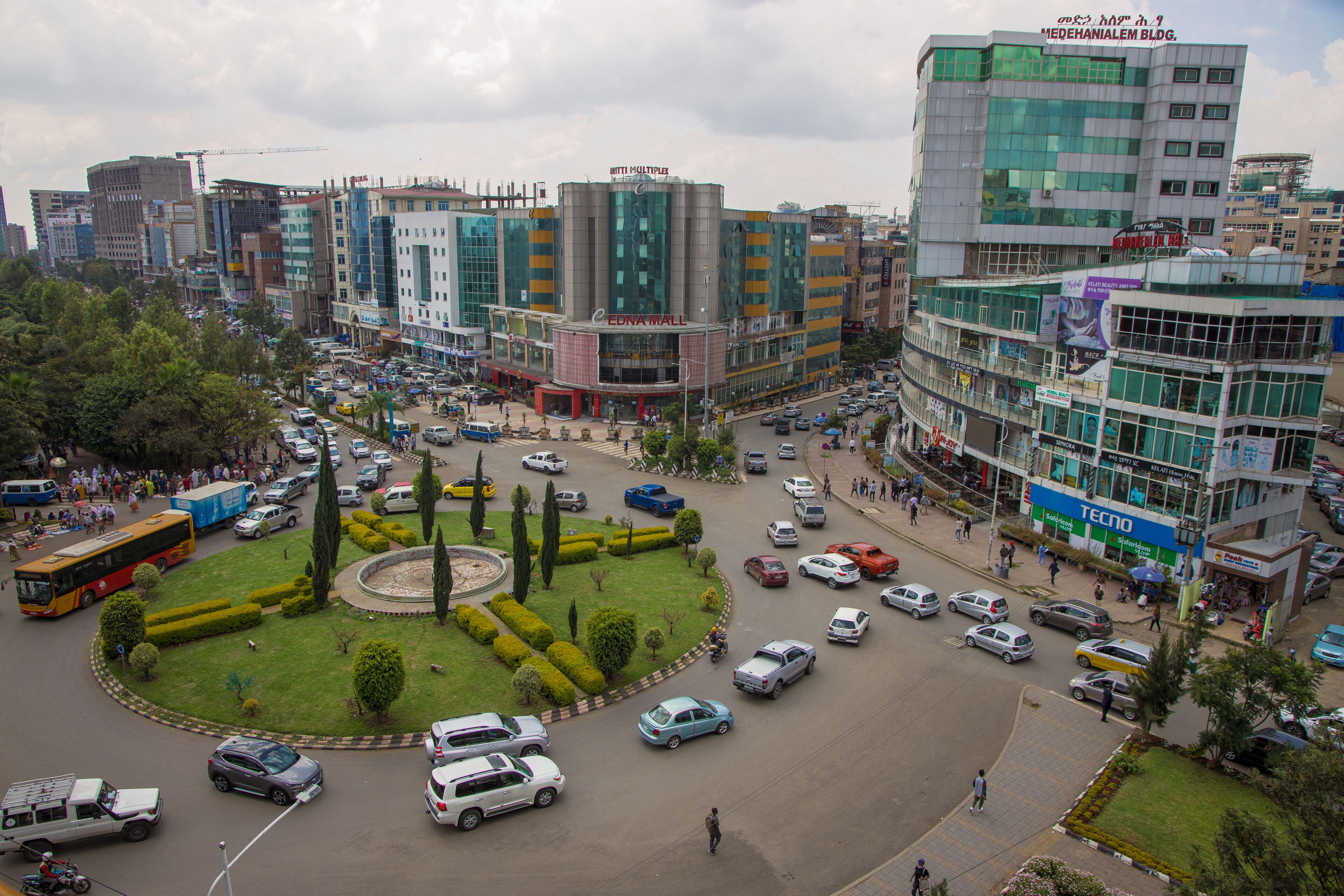 A busy urban intersection with multiple buildings, including a prominent multi-story structure with a glass facade and signage for a hotel.