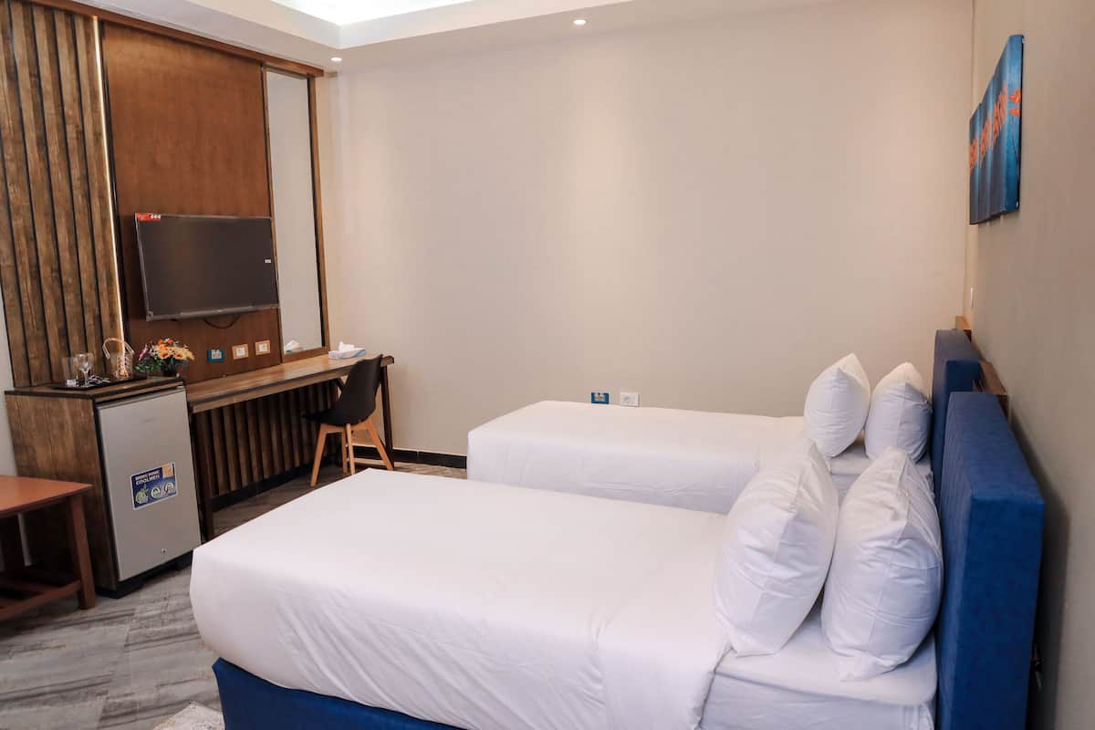 Une chambre d’hôtel avec deux lits, un bureau, une télévision et un petit réfrigérateur.