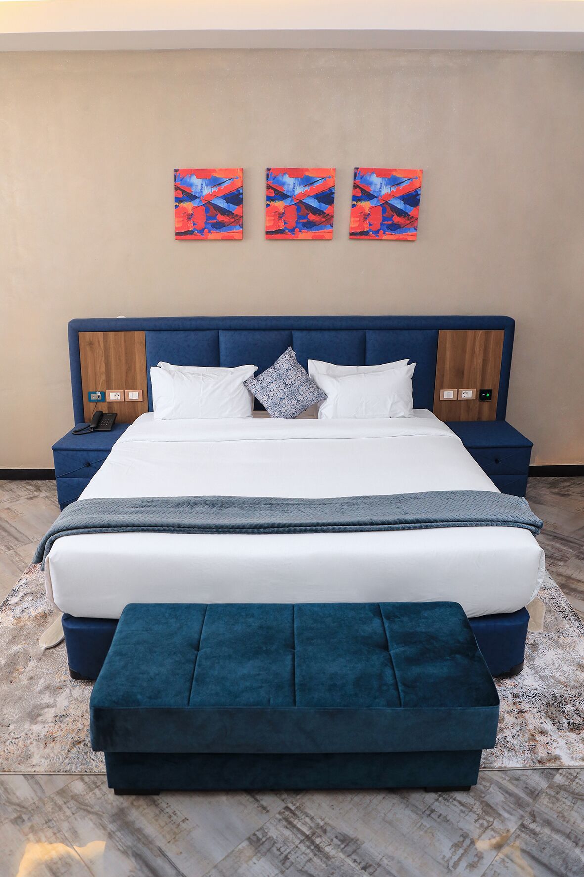 A modern bedroom with a large bed, two bedside tables, a headboard, and three abstract paintings on the wall.