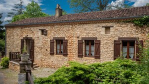 Un edificio in pietra con tetto in tegole, persiane di legno e un camino.