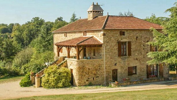 A stone building with a red-tiled roof, a small tower, and a covered porch.