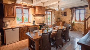 A rustic kitchen with wooden cabinets, a dining table set for six, and a stone wall.