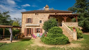 A stone house with a wooden porch, a staircase, and a small garden.