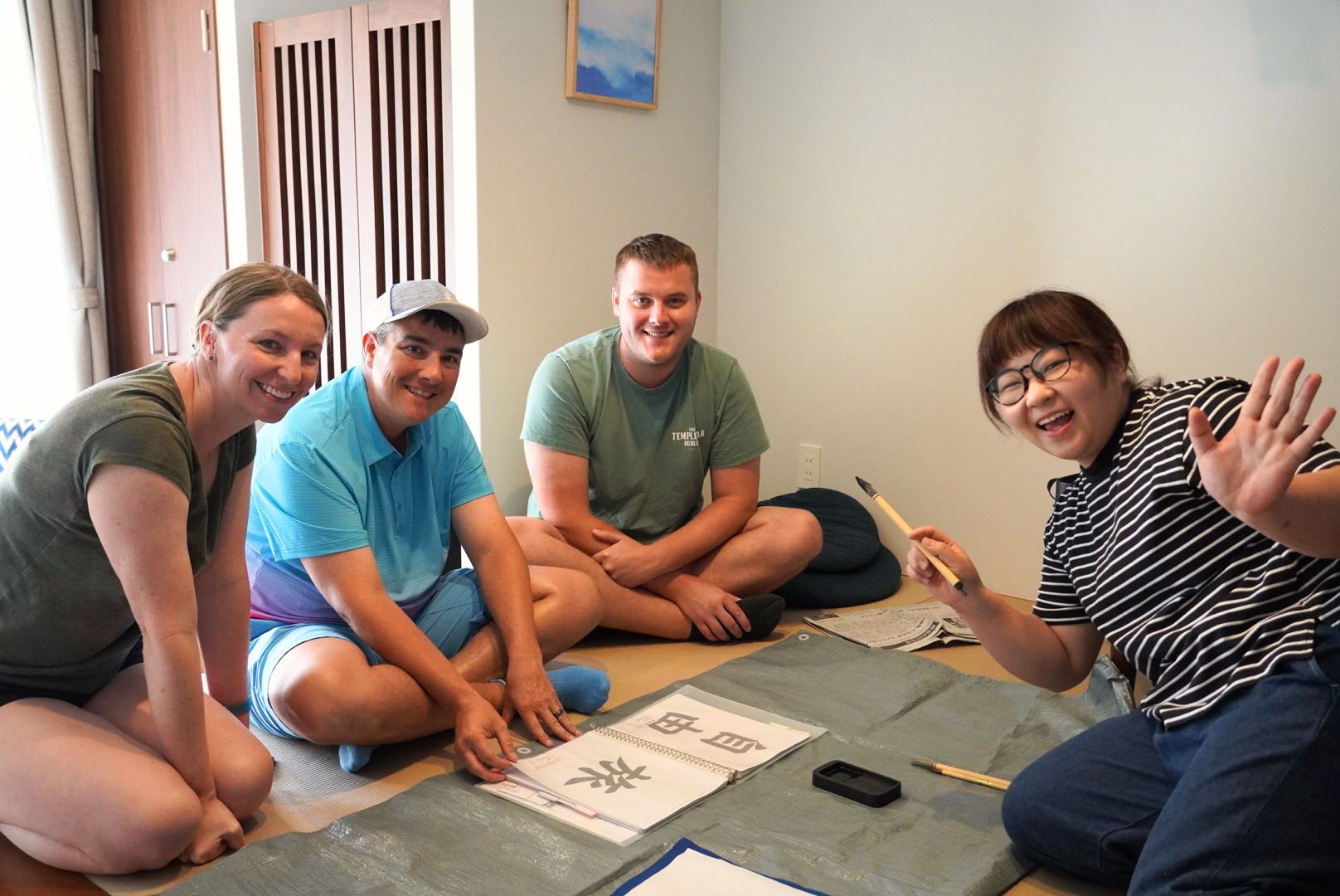 Four people sitting on the floor with a mat, surrounded by papers and a pen, in a room with a door and a window.