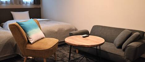 A hotel room with a bed, a sofa, a chair, and a small table.