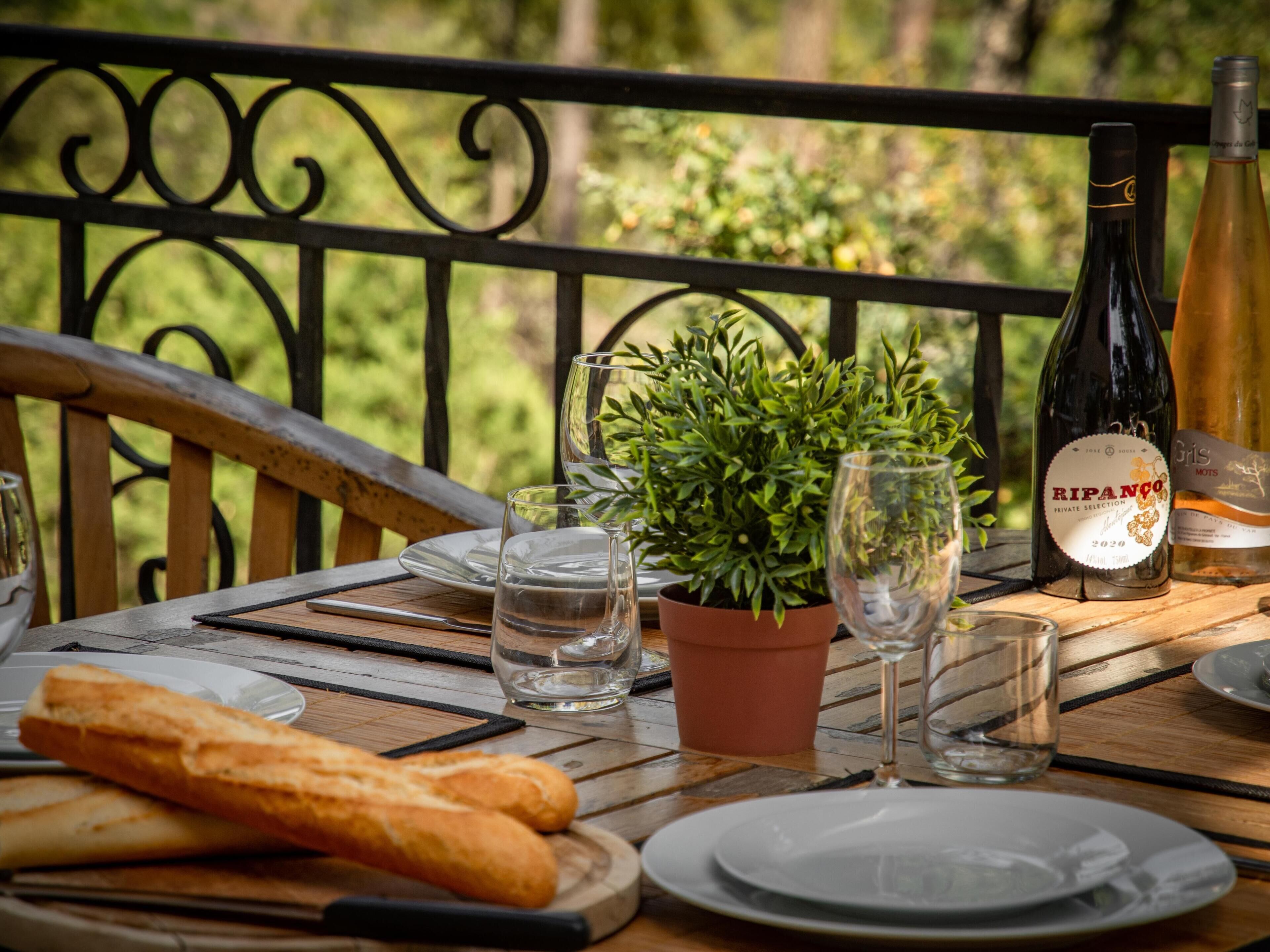 Une table en bois avec une plante en pot, des bouteilles de vin, des verres et du pain.