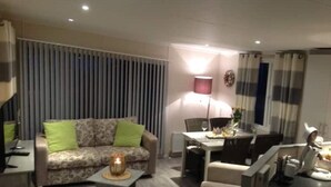 En moderne stue med sofa, lænestole, spisebord og lampe.