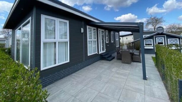 Et moderne hus i to etager med store vinduer og en overdækket terrasse.