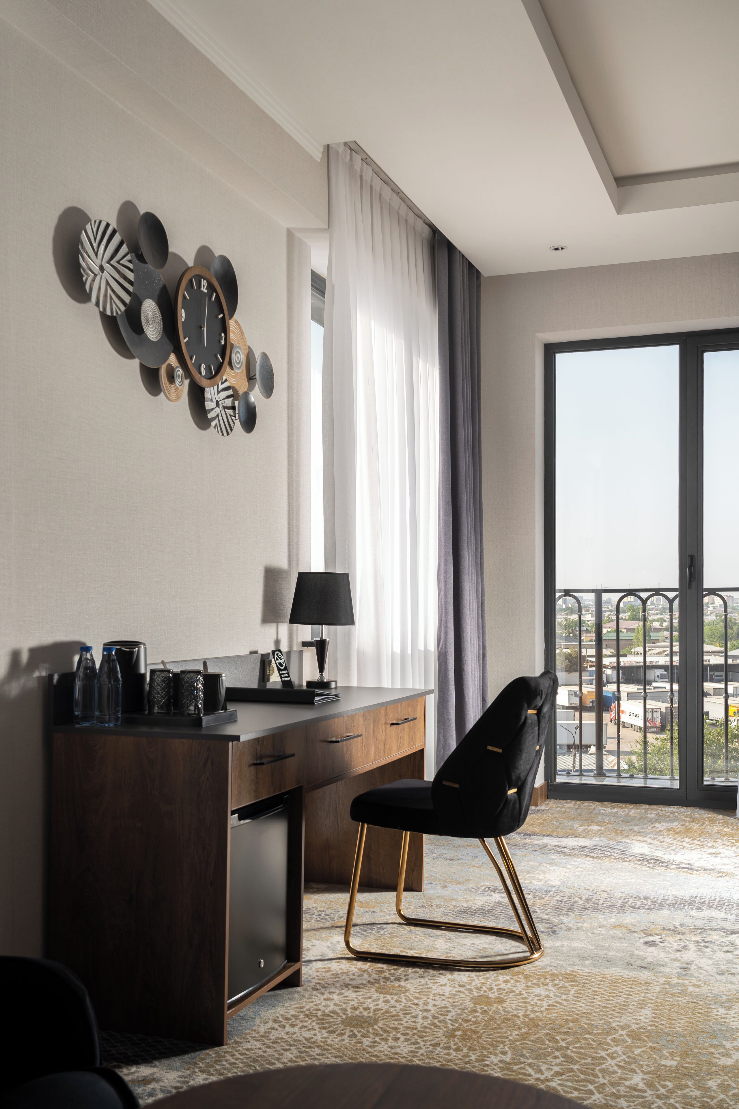 A modern hotel room with a desk, chair, and a large window offering a city view.