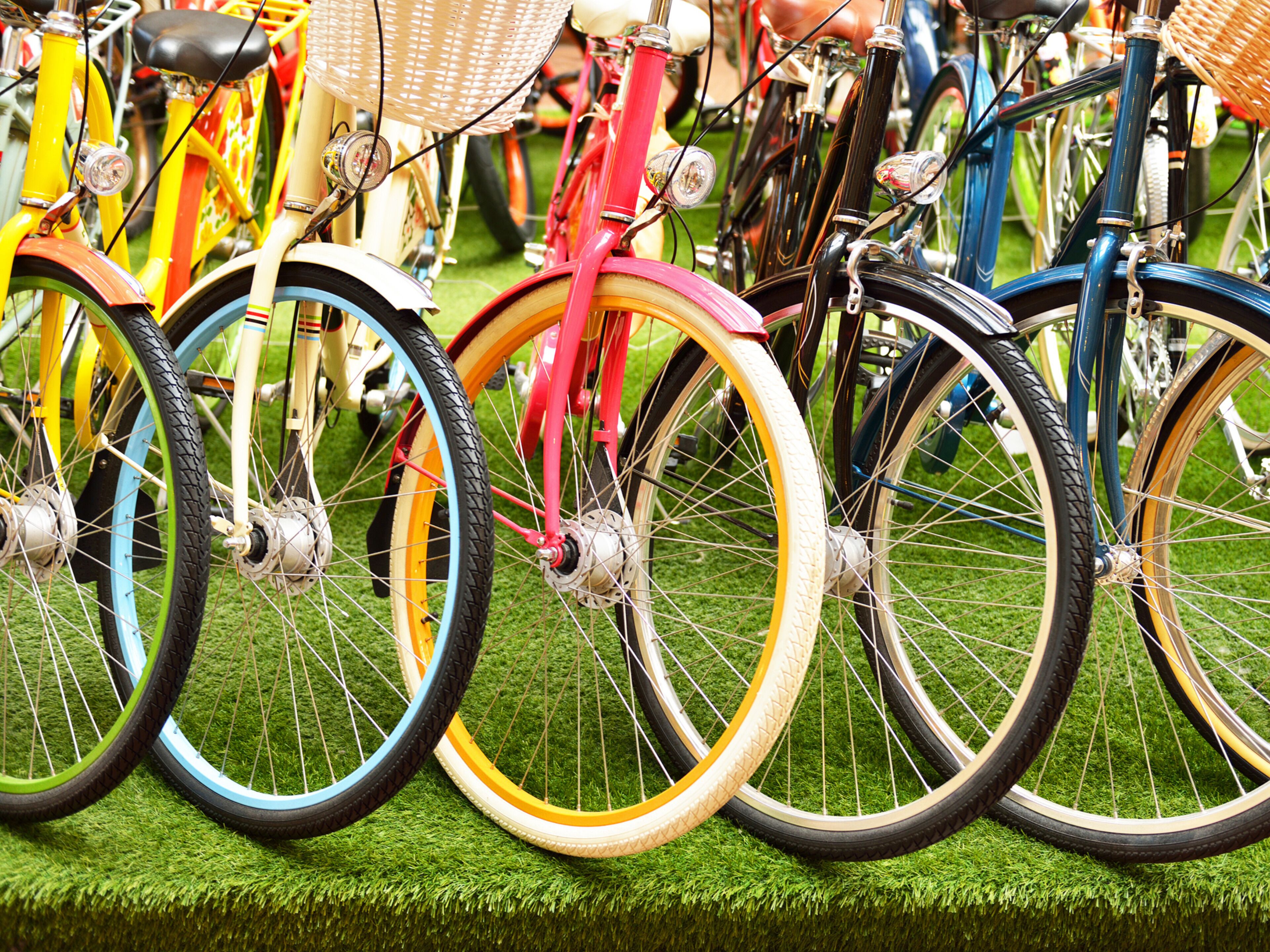 Varias bicicletas con ruedas y cestas de colores, estacionadas sobre césped.