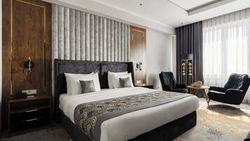 A modern hotel room with a large bed, a nightstand, a chair, a small table, and a lamp.
