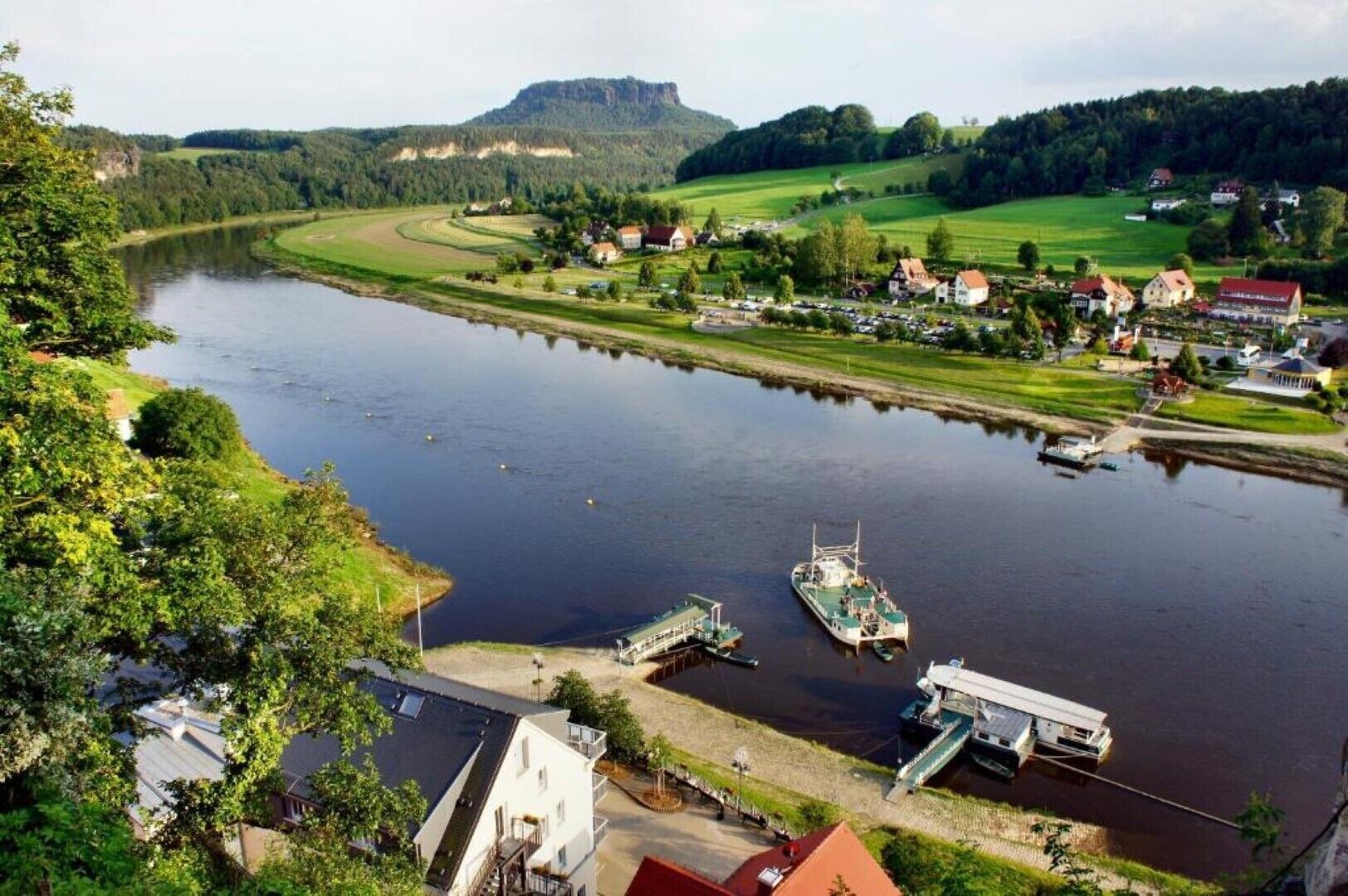 En stad vid en flod med båtar förtöjda, en bro och hus längs flodstranden.