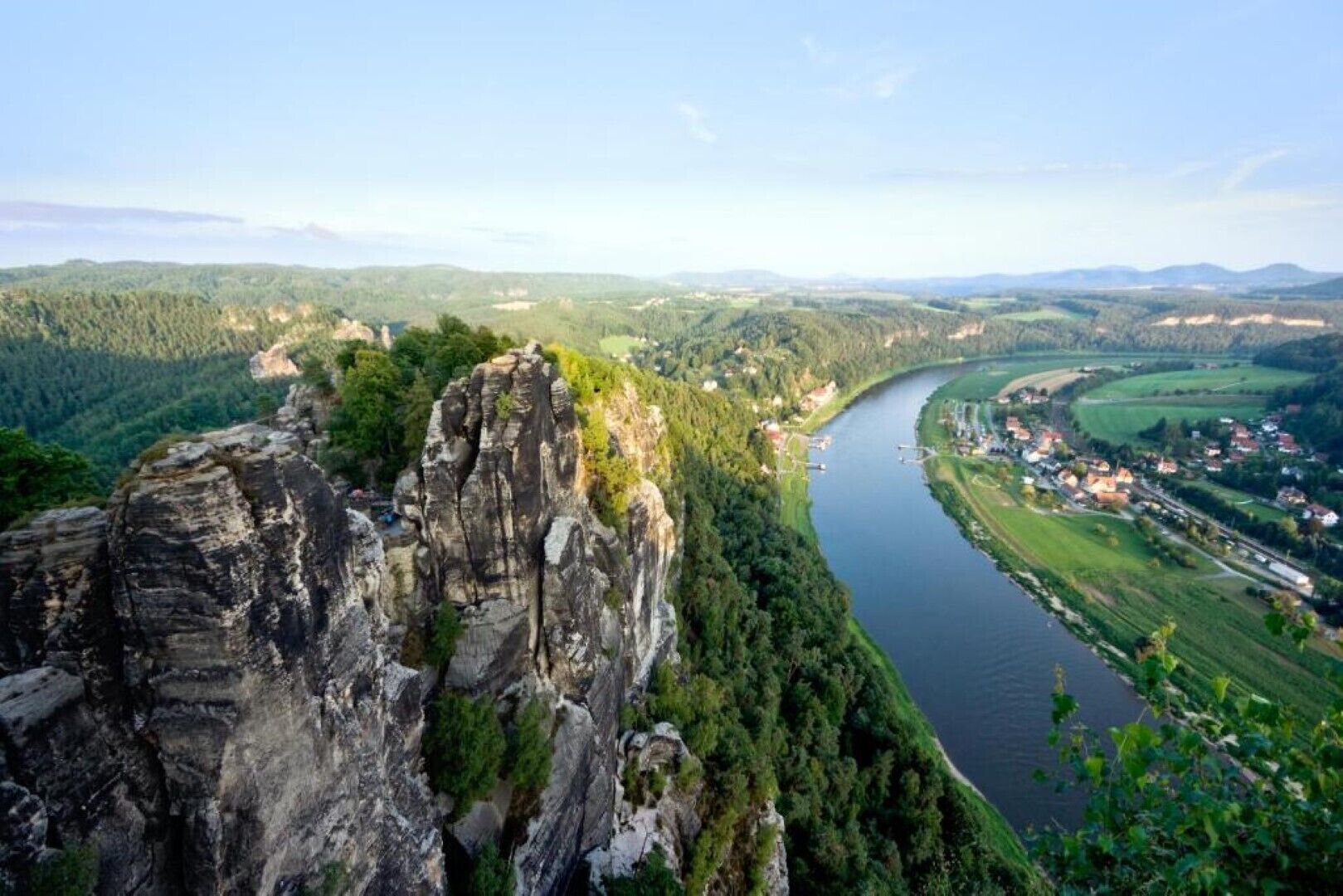 Ein Fluss fließt durch ein Tal, mit einer markanten Felsformation am linken Ufer.