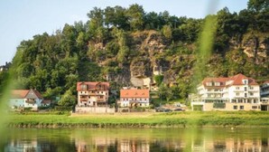 Un hôtel situé au bord d’un lac, composé de plusieurs bâtiments, dont le reflet se mire dans l’eau, avec une colline boisée en arrière-plan.