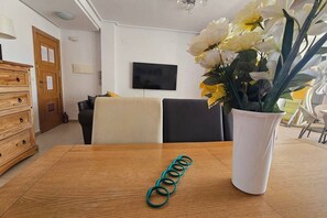 A dining area with a wooden table, a teal coiled object, and a white vase with flowers. - A bright pool views apartment - CO1011LT (Torre-Pacheco)