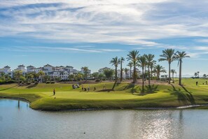 A golf course with a water hazard, palm trees, and buildings in the background. - A bright pool views apartment - CO1011LT (Torre-Pacheco)