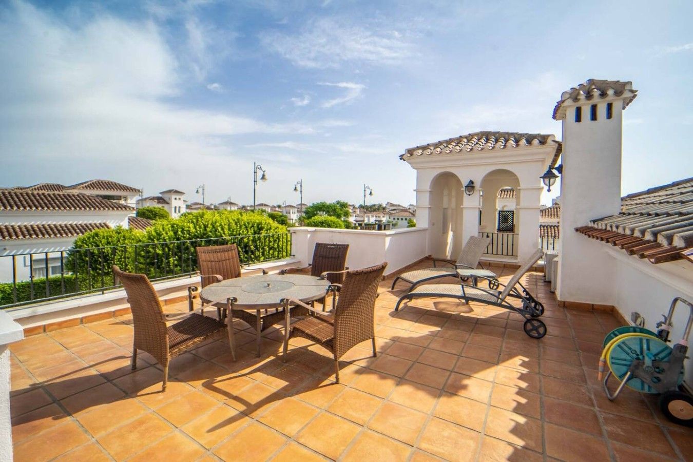 Une terrasse sur le toit avec une table et des chaises, une poussette et un petit bâtiment doté d’arcades.
