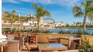 A rooftop terrace with wicker furniture, a view of a lake, and buildings with a Mediterranean architectural style. - Villa with private pool - CA13LT (La Torre Golf Resort)
