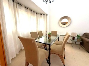 A dining area with a glass table and chairs, a round mirror on the wall, and a sofa in the background. - Villa with private pool - CA13LT (La Torre Golf Resort)