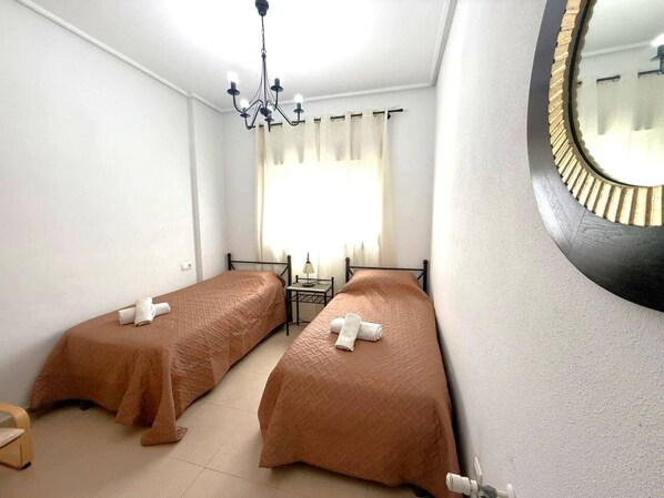 A room with two beds, a chandelier, a small table with a lamp, and a round mirror on the wall. - Villa with private pool - CA13LT (La Torre Golf Resort)