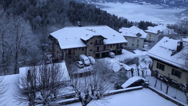 Un village de montagne enneigé, avec des bâtiments de style chalet traditionnel, une vue dégagée sur les montagnes environnantes et un paysage hivernal paisible.