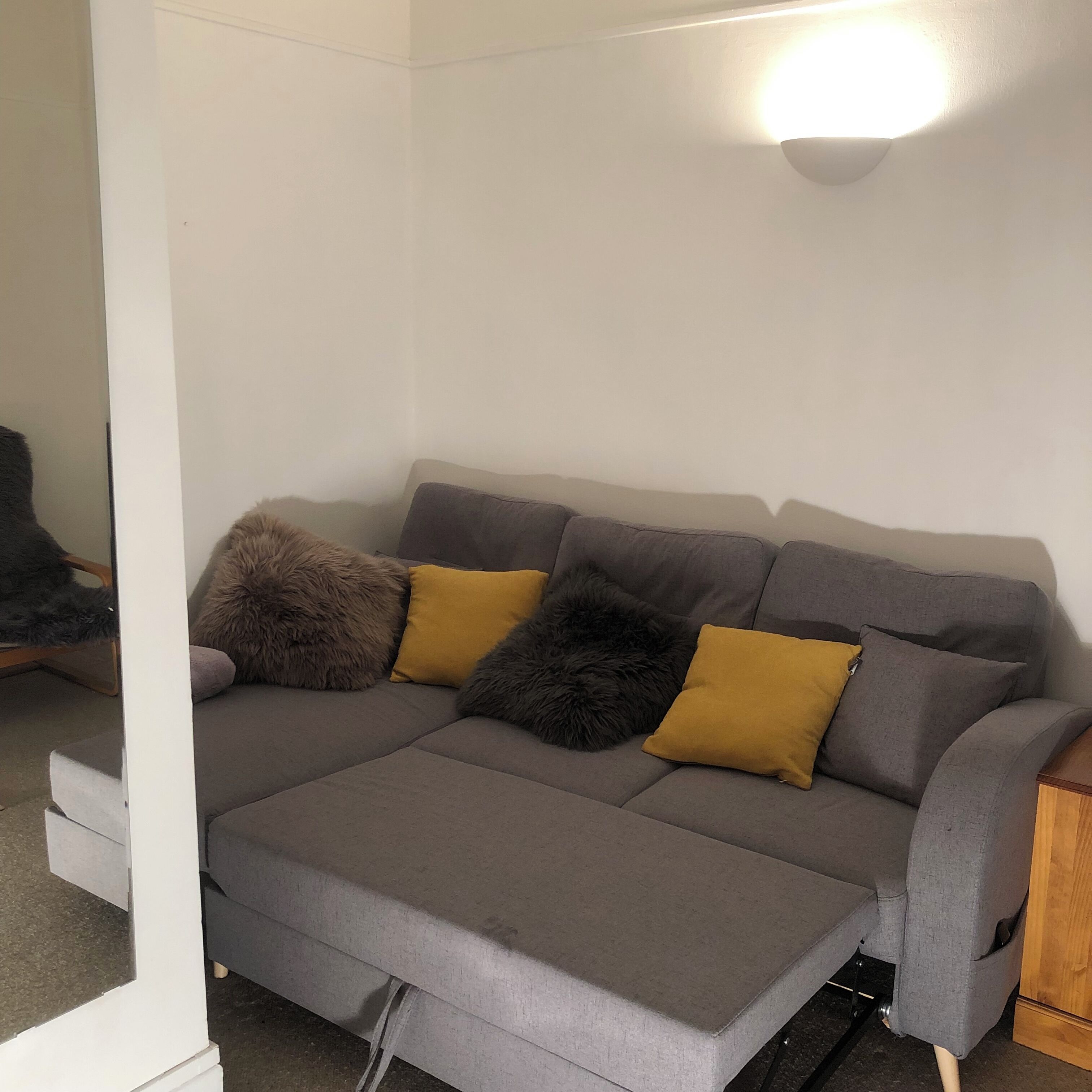 A grey sofa with a footrest, two mustard-colored cushions, and a fluffy grey pillow.