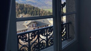 Une fenêtre donnant sur des montagnes enneigées, un balcon orné de balustrades en métal ouvragé et un bâtiment doté d’un toit en pente.