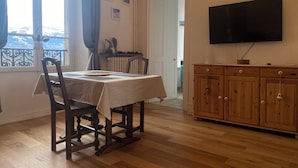 Un coin repas avec une table dressée pour deux personnes, un buffet en bois et un téléviseur fixé au mur.