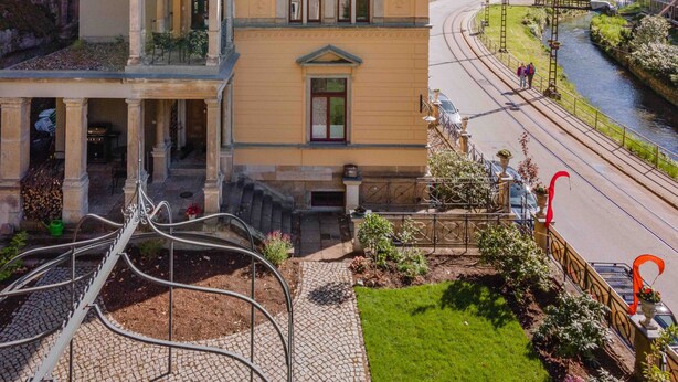 A two-story building with a balcony, a garden, and a view of a river and railway tracks. - Modern apartment 1 in Villa Emma for 2-4 people (Bad Schandau)
