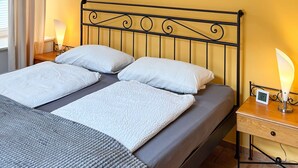 A bed with a metal headboard, two bedside tables with lamps, a wall clock, and a window with curtains. - Modern apartment 1 in Villa Emma for 2-4 people (Bad Schandau)