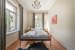 Een slaapkamer met een metalen bedframe, een zwart-wit vloerkleed, een kroonluchter en een schilderij aan de muur.