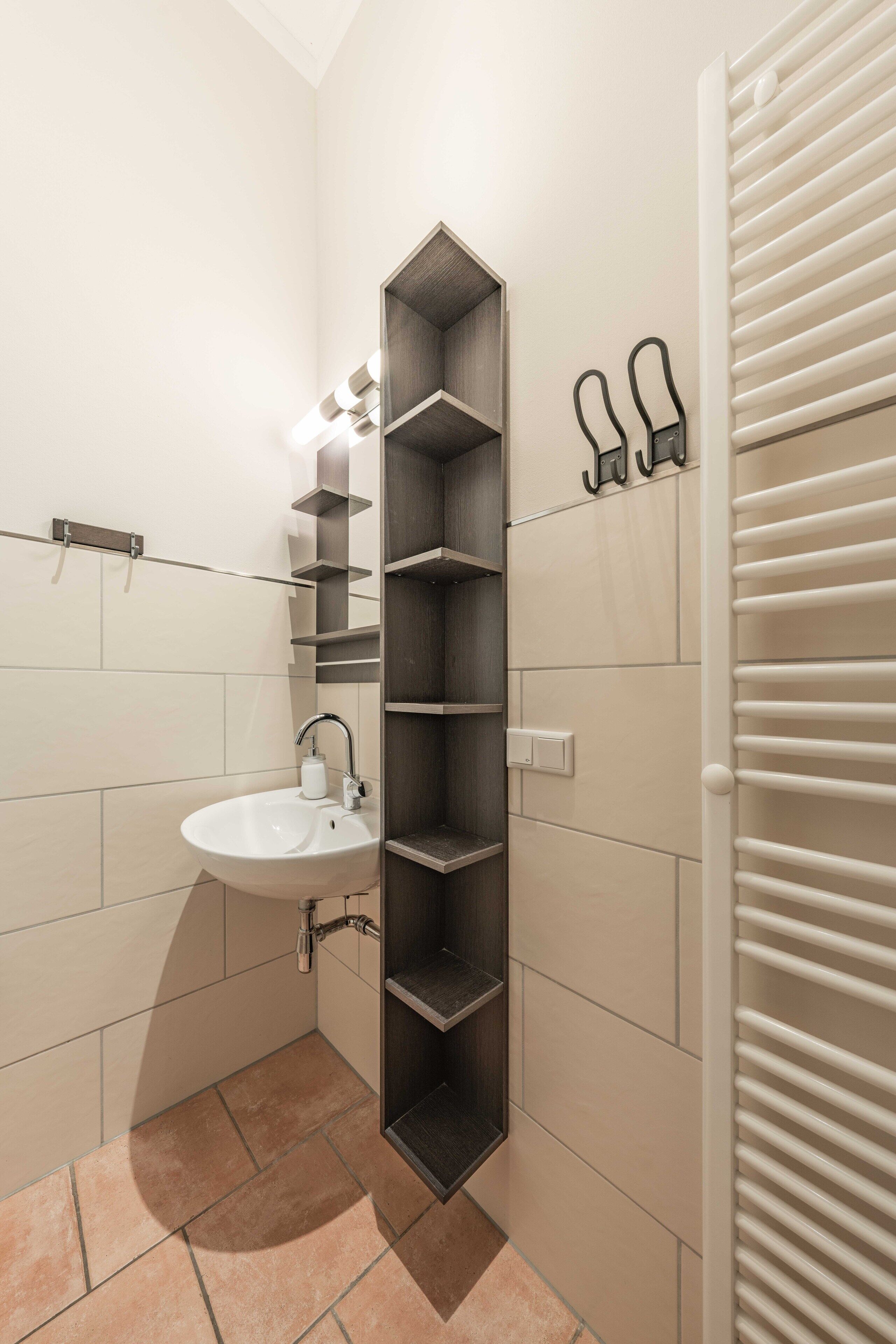 Casa de banho com lavatório branco, estante vertical e suporte para toalhas.