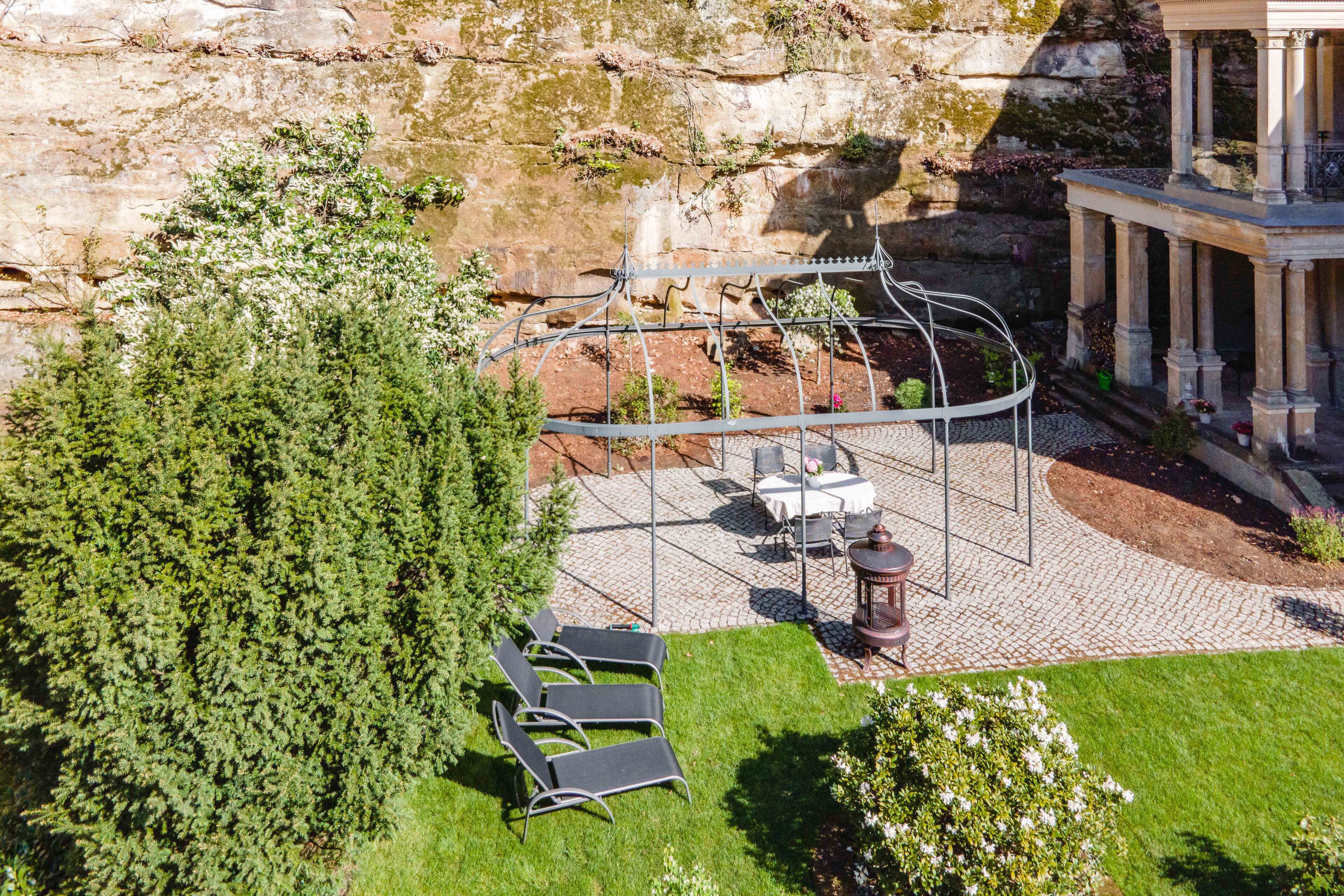 A rooftop garden with a pergola, seating area, and a view of a rocky cliff.