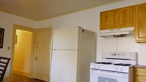 Una cocina con un refrigerador blanco, estufa, armarios de madera y una puerta que da a otra habitación.