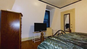 Un dormitorio con cama, televisor sobre un mueble, armario y puerta con espejo.