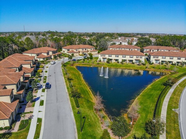 Un quartier résidentiel avec un étang central, des maisons aux toits recouverts de tuiles rouges et un ciel dégagé.
