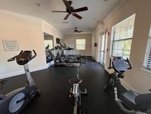 Une salle de sport équipée de nombreuses machines d’exercice, de ventilateurs de plafond et de grandes fenêtres.