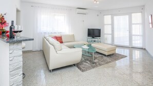 A modern living room with a sofa, a glass coffee table, and a flat-screen TV. - Apartments Andelic (Vir)