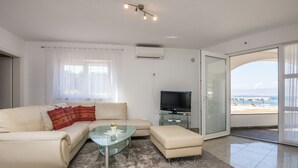A modern living room with a beige sofa, a glass coffee table, and a flat-screen TV. - Apartments Andelic (Vir)