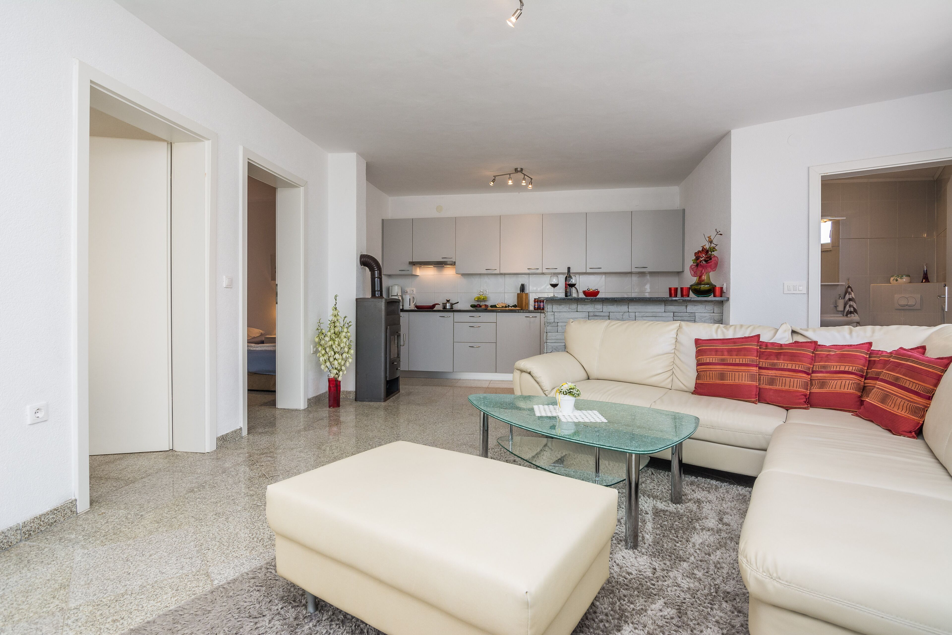 A modern living room with a glass coffee table, a beige sofa, and a kitchen in the background.