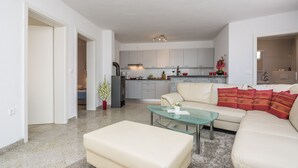 A modern living room with a glass coffee table, a beige sofa, and a kitchen in the background. - Apartments Andelic (Vir)