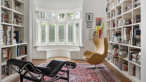 Una biblioteca con estanterías, un sillón de lectura, una ventana y una alfombra.
