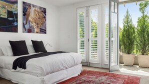 Un dormitorio con una cama, un tapete rojo estampado, paredes blancas y un ventanal con vistas a árboles.