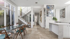 Una cocina moderna con encimera de mármol, un comedor con mesa de vidrio y sillas de madera, y una escalera que lleva a otro nivel.
