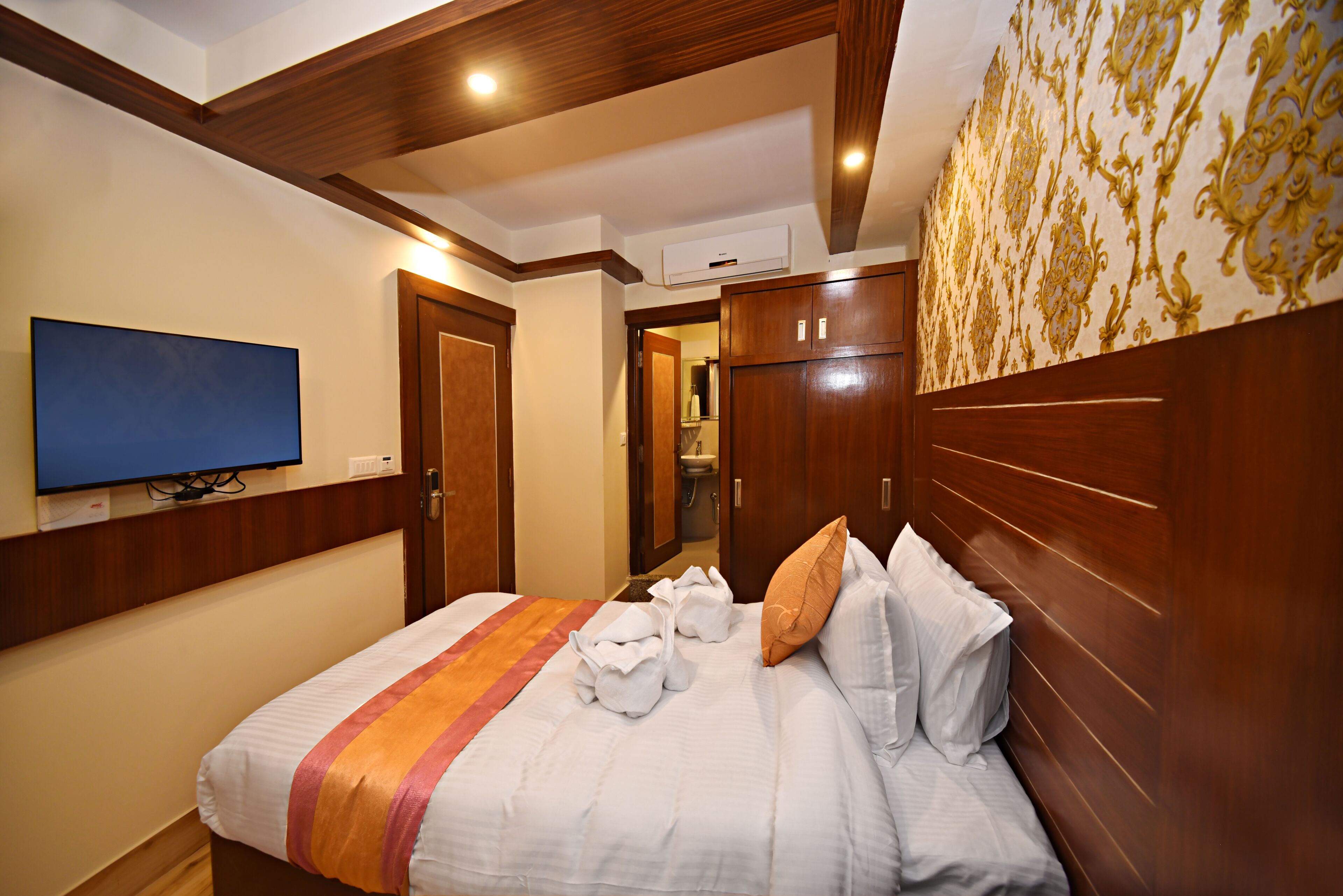 A hotel room with a bed, a television, wooden paneling, and a patterned wall.