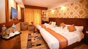 A hotel room with two beds, a TV, a desk with a tray of breakfast items, and a patterned rug. - Hotel Simal (Kathmandu)