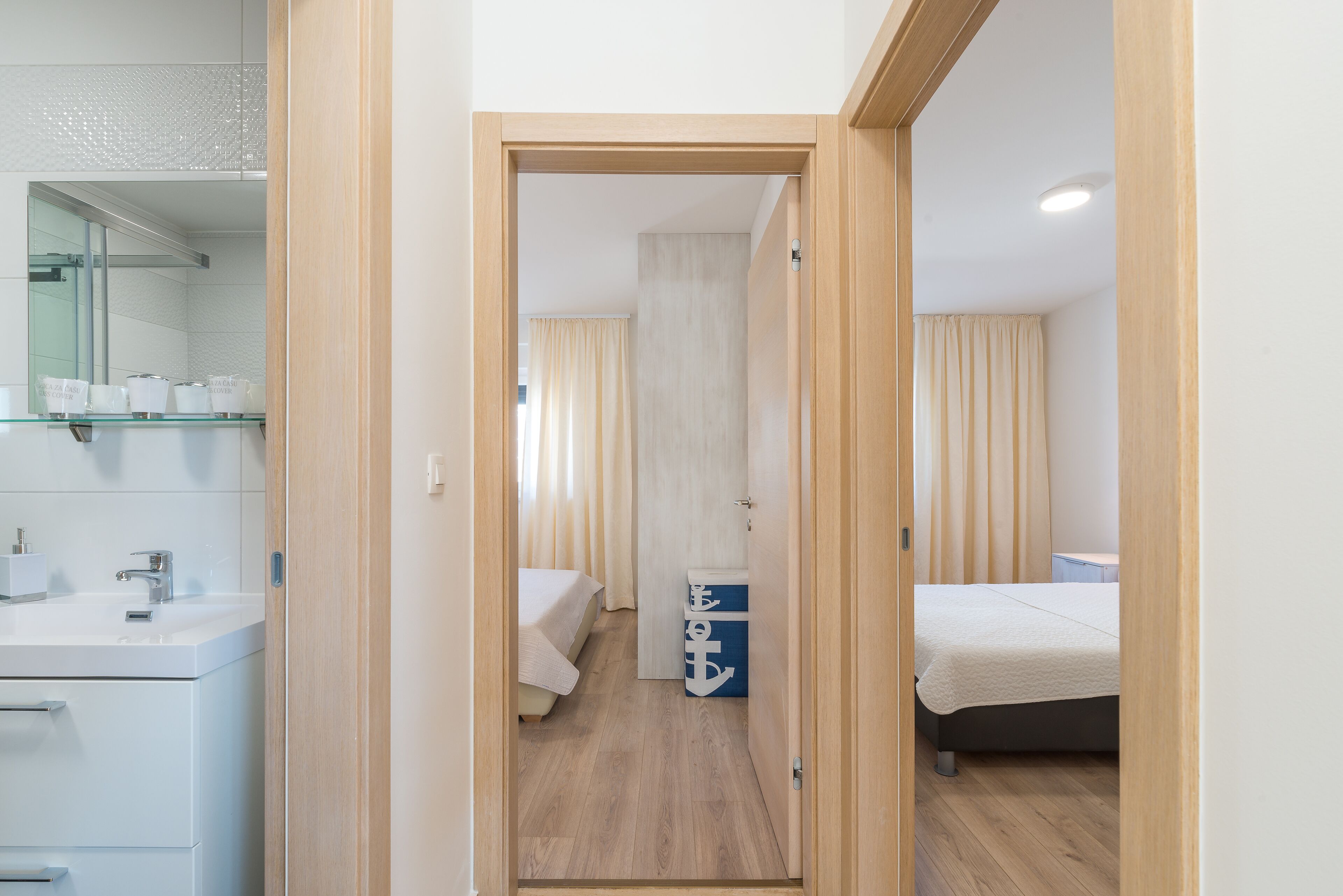 A hotel room with a wooden floor, a bed, a bedside table, a small desk, and a bathroom with a sink and mirror.