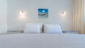 Uma cama bem arrumada com lençóis brancos, duas mesas de cabeceira e um quadro na parede retratando uma paisagem iluminada pela lua.