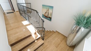 Uma escada de madeira com corrimãos de metal, um quadro de um veleiro na parede e uma grande planta em vaso.