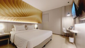 A modern hotel room with a large bed, bedside tables, a desk, and a flat-screen TV mounted on the wall.
